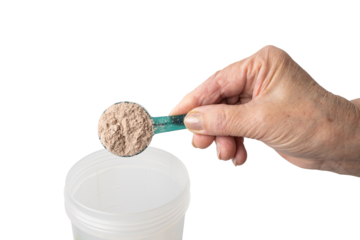 Senior female hand putting a portion of whey protein powder from a measuring spoon into a shaker, preparing a protein drink. Isolated on a transparent background