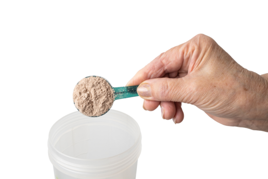 Senior female hand putting a portion of whey protein powder from a measuring spoon into a shaker, preparing a protein drink. Isolated on a transparent background