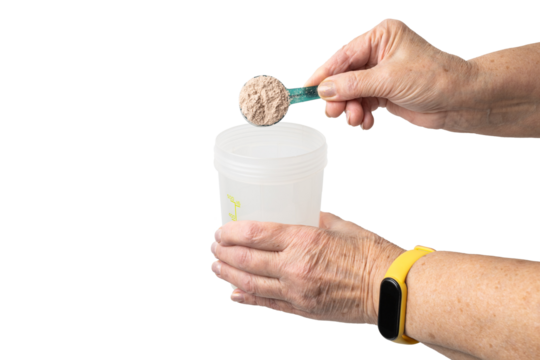 Senior female hand putting a portion of whey protein powder from a measuring spoon into a shaker, preparing a protein drink. Isolated on a transparent background