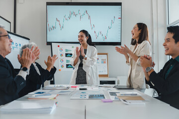 Happy business team clapping hands during a meeting in an office conference room, celebrating the successful outcome of a project, with charts and graphs displayed on a screen and whiteboard