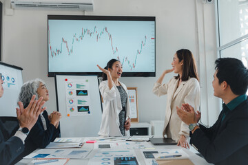 Enthusiastic businesswomen giving high five while celebrating successful financial results with their team in the meeting room, showing positive growth and achievement in business