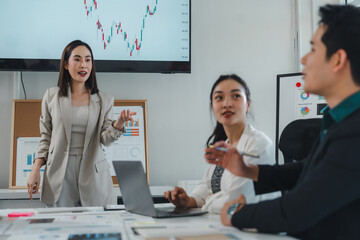 Business team engaging in a lively discussion about charts and graphs projected on a screen and pinned to a board, led by an asian businesswoman during a collaborative meeting