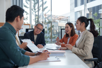 Asian business team collaborating in a modern office, discussing strategies and analyzing financial figures on a clipboard while brainstorming ideas for a new project