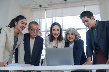 Obraz premium Diverse colleagues are collaborating on a project, gathered around a laptop in a modern office meeting room, engaging in teamwork and utilizing technology