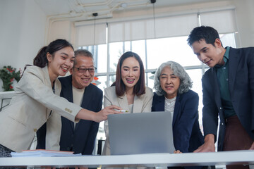 Diverse professionals, including senior and junior members, collaborating on a project and engaging in productive discussions around a laptop in a modern office