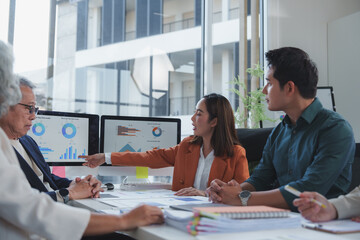 Fototapeta premium Businesswoman pointing at charts on a computer screen while leading a discussion during a meeting with colleagues in a modern office environment, fostering teamwork and collaboration