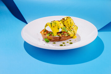 Delicious eggs benedict served on toast with vibrant yellow sauce and green garnish against a bright blue backdrop