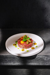 Delicious beef tartare served on a white plate with vibrant garnishes and drizzles in a modern setting during daylight