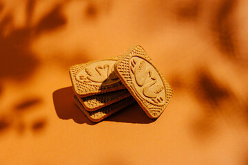 Delightful cookies stacked on a warm orange background with intricate designs and soft shadow play