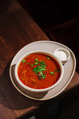 Delicious bowl of spicy tomato soup garnished with fresh herbs served on a wooden table