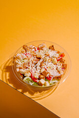 Fresh salad with croutons and cheese on a vibrant yellow background displayed in a clear bowl