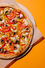 Delicious vegetarian pizza topped with fresh vegetables and vibrant colors on a bright orange background