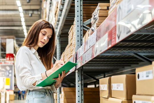 Focused on her task, a young woman holding clipboard meticulously updates inventory records while surrounded by shelves filled with various products in a vibrant warehouse setting