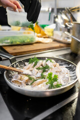 A chef prepares a creamy mushroom dish in a modern kitchen. Fresh herbs are added for flavor, showcasing the art of cooking and fresh ingredient use in culinary creations.