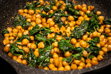 fried Mediterranean middle eastern chickpeas with spinach in frying pan skillet on home kitchen stove. delicious tasty vegan health food pulses and leafy green vegetable