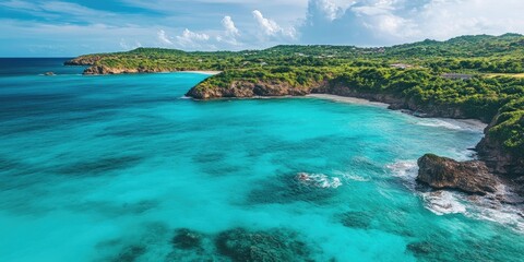 Fototapeta premium Turquoise coastal landscape featuring vibrant blue waters, lush green hills in the background, with rocky shores and scattered clouds in a clear sky.