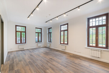 A bright empty room in the mansion. Windows with brown frames, dark laminate. Unfurnished.