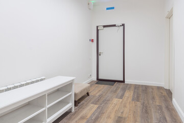Entrance hall with white room decoration. Dark laminate. The front door. A white shoe shelf and a small ottoman.
