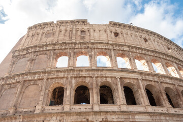 Fototapeta premium Facade and exterior of the ancient Roman Colosseum in Rome, Italy with its arches on a sunny day with white clouds and blue sky