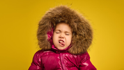 Portrait of five years old girl, emotional child in pink warm coat with large fur hood grimacing...