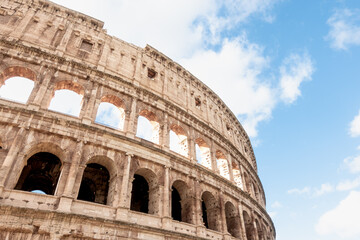 Fototapeta premium Facade and exterior of the ancient Roman Colosseum in Rome, Italy with its arches on a sunny day with white clouds and blue sky