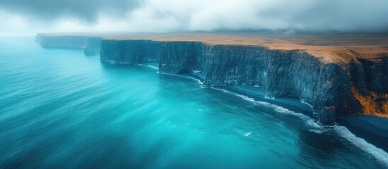 Fototapeta premium Stunning aerial view of the dramatic southern coastline of Iceland showcasing turquoise waters and rugged cliffs under a moody sky