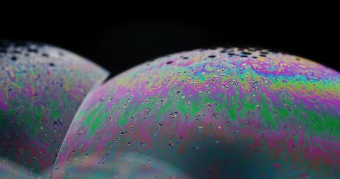 camera slowly zooming in on complex patterns on surface of soap bubble. small dots with different film thickness floating to top
