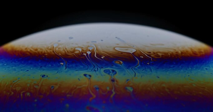 Planet looking soap bubble exhibiting complex structures and vibrant rainbow colors in it's vapor like surface film