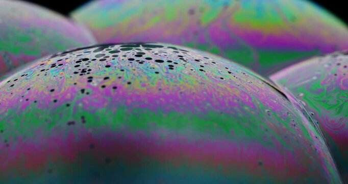 Dark dots levitating to top of soap bubble, as complex color patterns swirl across the surface of the complex soap film