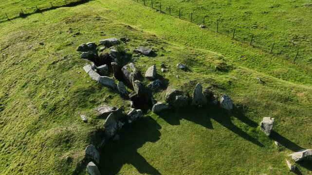 Ballymacdermott Court Tomb, County Armagh, Northern Ireland, October 2022. Drone orbits counter clockwise of the cicular neolithic site with sunlight casting casting shadows on the ancient stones.
