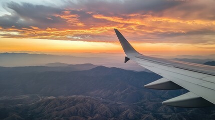 Obraz premium An aerial view of distant mountain peaks and rolling hills at sunset, with vibrant golden tones and dramatic clouds painting the sky from an airplane window.