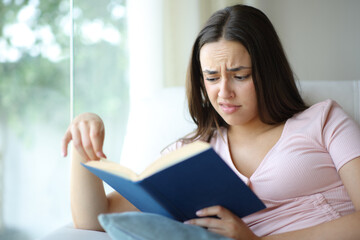 Confused woman reading a paper book at home
