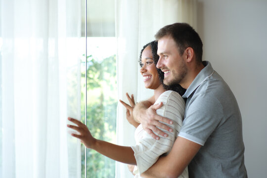 Happy interracial couple at home contemplating outside