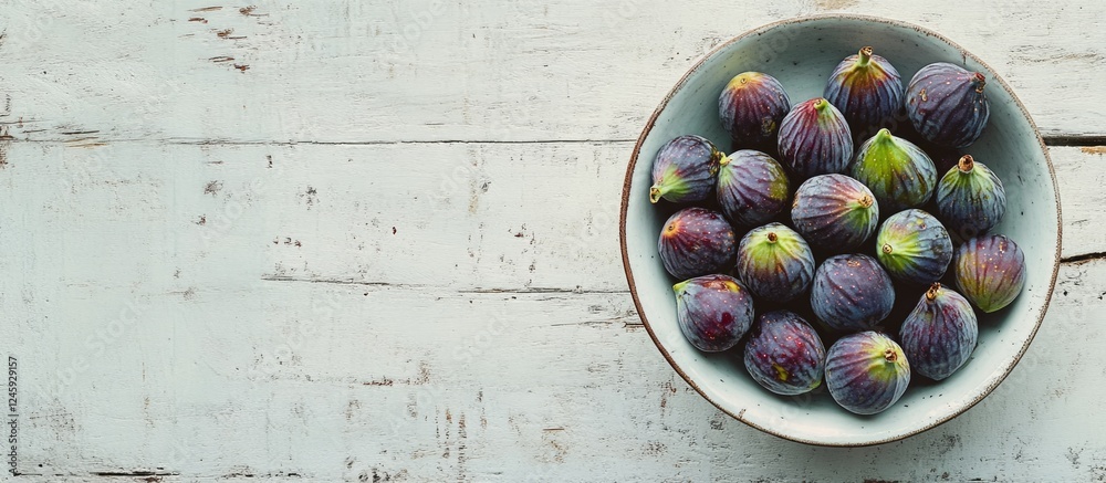 Poster bowl of fresh ripe figs arranged on a textured white table in a flat lay style showcasing their natu