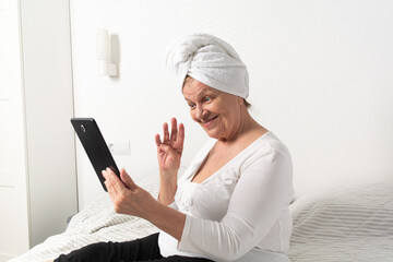 Caucasian senior woman with wrinkles talking with somebody by tablet