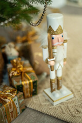 A white and gold nutcracker stands by a Christmas tree