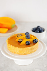 Homemade mango tart with blueberry and chia seeds on a stand on a table. Sugar, sugar substitutes, lactose and gluten free. Vegan dessert. Vertical orientation.