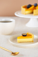 Piece of vegan mango pie or tart with fresh blueberry, mousse from coconut milk and cup of tea. Sugar, sugar substitutes, lactose and gluten free. Vertical orientation.