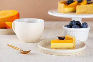 Piece of homemade vegan mango pie or tart with fresh blueberry, mousse from coconut milk and cup of tea. Sweet breakfast. Sugar, sugar substitutes, lactose and gluten free.