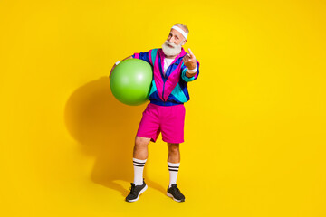Full length photo of cheerful positive mature guy dressed retro sport jacket holding fit ball showing you isolated yellow color background