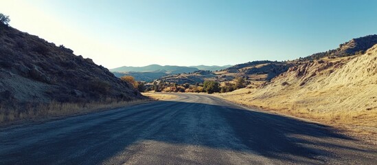 Asphalt Road Leading into Scenic Foothills with Blue Sky and Open Space for Text Display