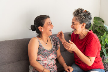 Two happy women laughing together on sofa in living room