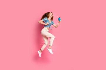 Happy young woman jumping with coffee on pink background