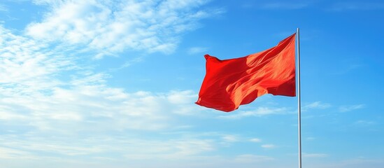 Red flag fluttering in the breeze under a clear blue sky creating an ideal backdrop for promotional or informational text.