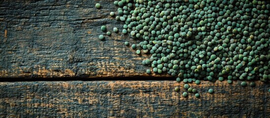 Fototapeta premium Green dry lentils scattered on rustic wood surface showcasing their texture in a top view close-up format for culinary and food photography.