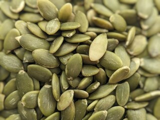 Close-up image of raw, green pumpkin seeds with a detailed and textured surface, showcasing their natural shape and color.