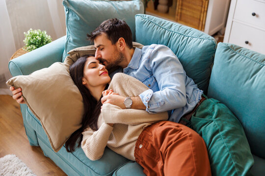 Couple relaxing at home cuddling on living room couch