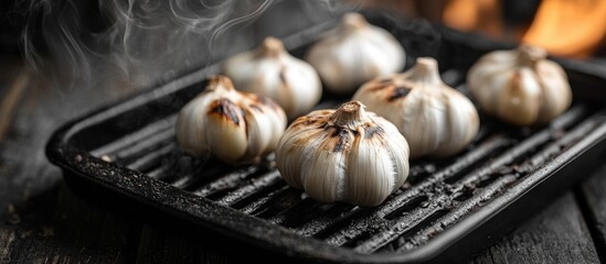 Grilled garlic cloves on a black wooden background with smoky atmosphere showcasing a rustic cooking scene.
