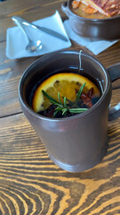 A cup of mulled wine with a slice of orange and rosemary in it
