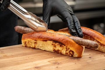Chef putting sausage in a hot dog bun for serving in a cafe
